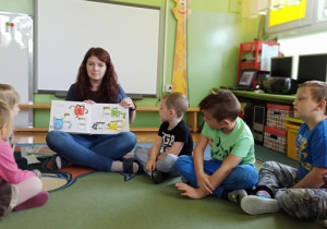 Dzieci słuchają i oglądają książkę "Kolorowy potwór"